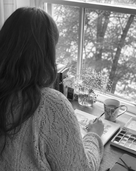 The artist at her studio window, painting watercolors in soft morning light